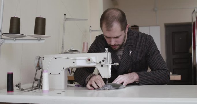 The tailor stitches clothes with sewing machine in a studio