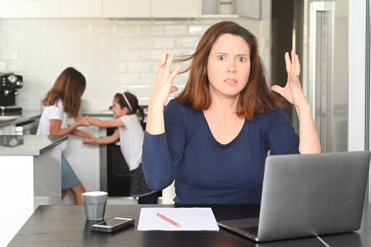 Upset mother working from home while children fight in the background