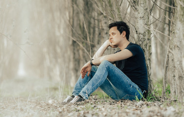 young man sitting by a tree in the woods thinking about life and resting. copy space