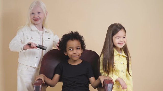Albino child girl combing curly hair of american boy isolated, girl brushing hair of cute boy sitting on chair.