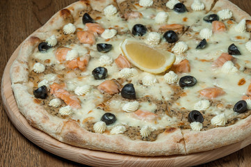 pizza on a wooden tray stands on a wooden table
