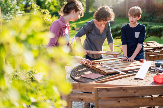 A mother and her two children build wooden planters for their permaculture vegetable garden