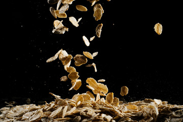 Whole oats being poured onto counter, oatmeal on a black background