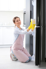 Woman in rubber gloves cleaning refrigerator at home