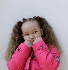 portrait of a little girl, little girl in a pink jacket meditates propping her face with her hands on a white background