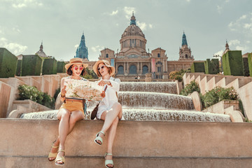 Two girlfriends are looking at a map of attractions in Barcelona and Spain. Tourism after Covid-19 quarantine and lockdown concept