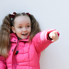 portrait of a little girl, little girl in a pink jacket of curly hair points somewhere in the...