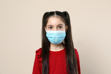 Little girl in medical mask on beige background. Virus protection
