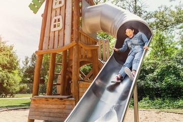 A girl rolls down a steep children's slide on the Playground. Concept of infantilism and personal...