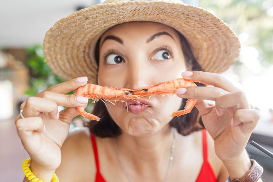Funny Asian girl makes a moustache out of fresh shrimp. Concept of Mediterranean cuisine and delicious seafood
