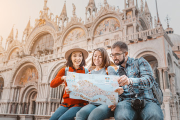 Multinational millennial friends discuss a travel plan with a sightseeing map of Italy's attractions. On San Marco square in Venice. The concept of tourism business after the pandemic coronavirus