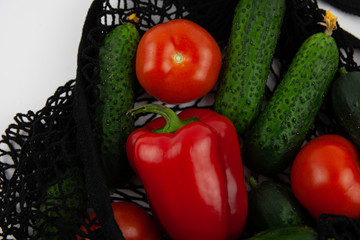Red fresh tomatoes and peppers, green fresh cucumbers in a reusable grocery bag. Healthy and conscious lifestyle