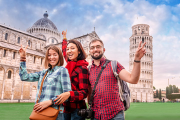 A fun and diverse group of young tourist friends pose against the backdrop of the famous leaning tower in Pisa. Tourism in Italy after canceling the quarantine and lockdown concept - obrazy, fototapety, plakaty