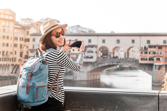 Girl travel blogger takes pictures as content for social networks and sites in Florence with a view of the famous bridge the Ponte De Vecchio