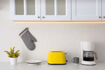 Modern toaster, coffeemaker and dishware on counter in kitchen