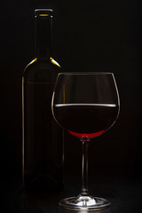 a glass and a bottle of wine standing on the table. vertical orientation on a dark background.