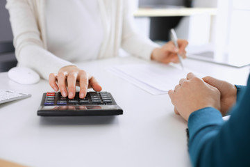 Accountant checking financial statement or counting by calculator income for tax form, hands closeup. Business woman sitting and working with colleague at the desk in office toned in blue. Tax and