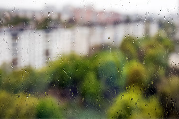 Close-up shot of rain drops on the window with blurred spring city landscape