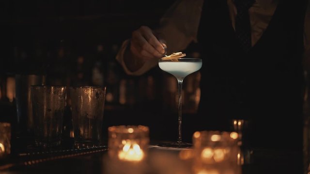 Real time medium shot of a bartender decorating a cocktail. Bartender preparing a cocktail at a bar in Bangkok, Thailand. Nightlife of a big city.