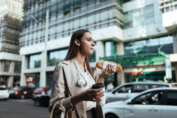 office worker at lunch break walks along the road and eats a sandwich and coffee - 344815484