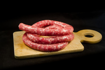 delicious fresh Italian pink pork sausage laid on a wooden cutting board on black  background