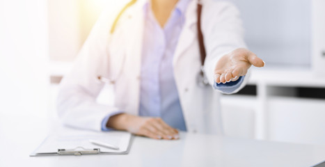 Unknown woman-doctor in blue blouse is giving helping hand while sitting at the desk in sunny clinic. Medicine concept