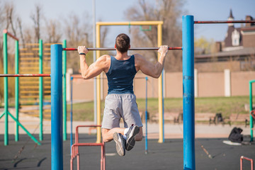 Young strong guy pulls himself up on the horizontal bar.