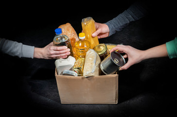Volunteers putting different products in donation boxes on dark background