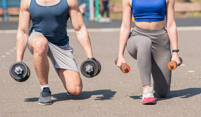 Fototapeta na wymiar Athletic guy and girl lunges with dumbbells at the playground. Health care.