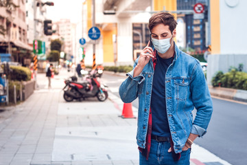 Fototapeta premium A mature handsome man with a beard talking on his mobile phone and wears a face pollution mask to protect himself from coronavirus on the street.