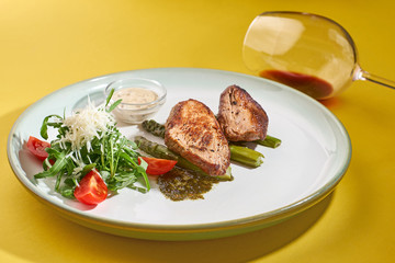 grilled pork meat with fresh vegetables salad and red wine on a yellow background