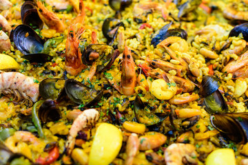 Close up of large portion of traditional Spanish paella dish freshly being cooked with seafood and pasta in a  frying pan at a street food festival, ready to eat seafood, side view, selective focus
