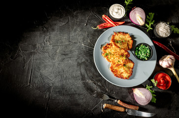 Potato pancakes with sour cream, herbs, garlic and spices on a dark background. Top view with copy space