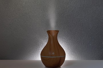 aromatic brown air humidifier with gray background and light around, turned on and releasing smoke...