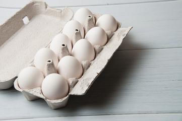 White chicken eggs in a tray on a light wooden background, copy space