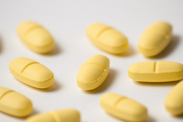 Yellow pills, antibiotics or vitamins on white background macro, close up