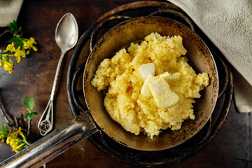 Hot corn porridge with sugar and butter on an old rustic pan and a metal vintage stand. Next to it is a sprig of flowering black currant with yellow flowers