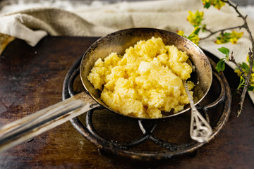 Hot corn porridge with sugar and butter on an old rustic pan and a metal vintage stand. Next to it is a sprig of flowering black currant with yellow flowers