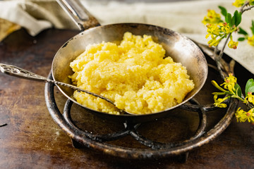 Hot corn porridge with sugar and butter on an old rustic pan and a metal vintage stand. Next to it is a sprig of flowering black currant with yellow flowers