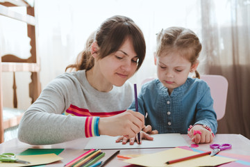 A mother with a child sits at the table and does homework. The child learns at home. Home schooling.