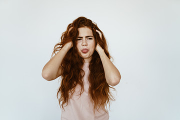Fototapeta premium disgusted sticking out her tongue girl rubs her hands with her luxurious red hair on a gray background