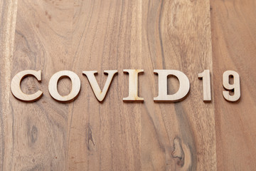 Wooden letters forming the word COVID19. The whole is arranged on a table in solid oak and a structurant light comes from above.