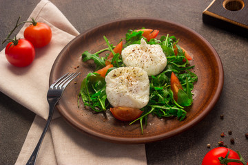 Poached eggs on lettuce and arugula, on a clay plate. Dark background