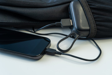 Smartphone charging with power energy bank in backpack on white wood board