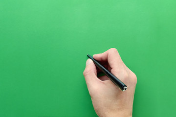 The hand holds a pen to write on a clear green background with a large space.. Concept of education and drawing