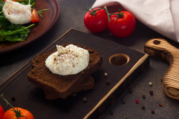 Healthy breakfast of toast with poached egg, tomatoes on a dark background