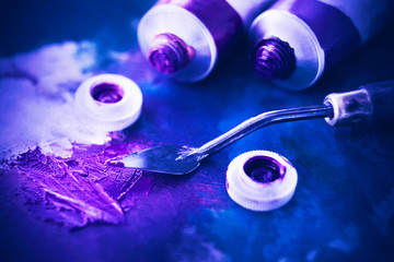 Open tubes of purple and blue oil paint lie on a blue background, and next to it lies a palette...