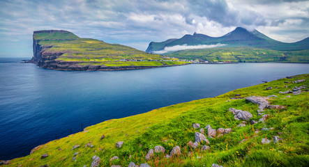 Naklejka na ściany i meble Dramatic summer view of Eidi village. Rainy morning scene of Eysturoy island. Green landscape of Faroe Islands, Denmark, Europe. Beauty of nature concept background.