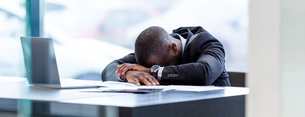 Tired African businessman sitting at the Desk in the office, fell asleep on the table. Hard day's...