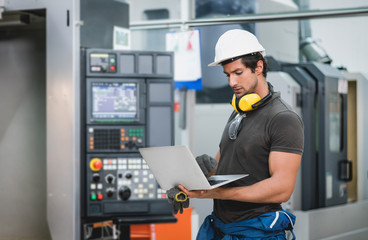 Engineer using laptop computer operating control CNC Machinery at factory Industrial